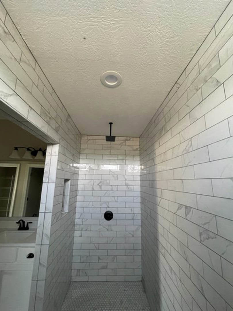 Modern bathroom featuring a glass-enclosed shower with white tile walls, a sleek white sink with chrome faucet, light plaster ceiling, and neutral tiled flooring.