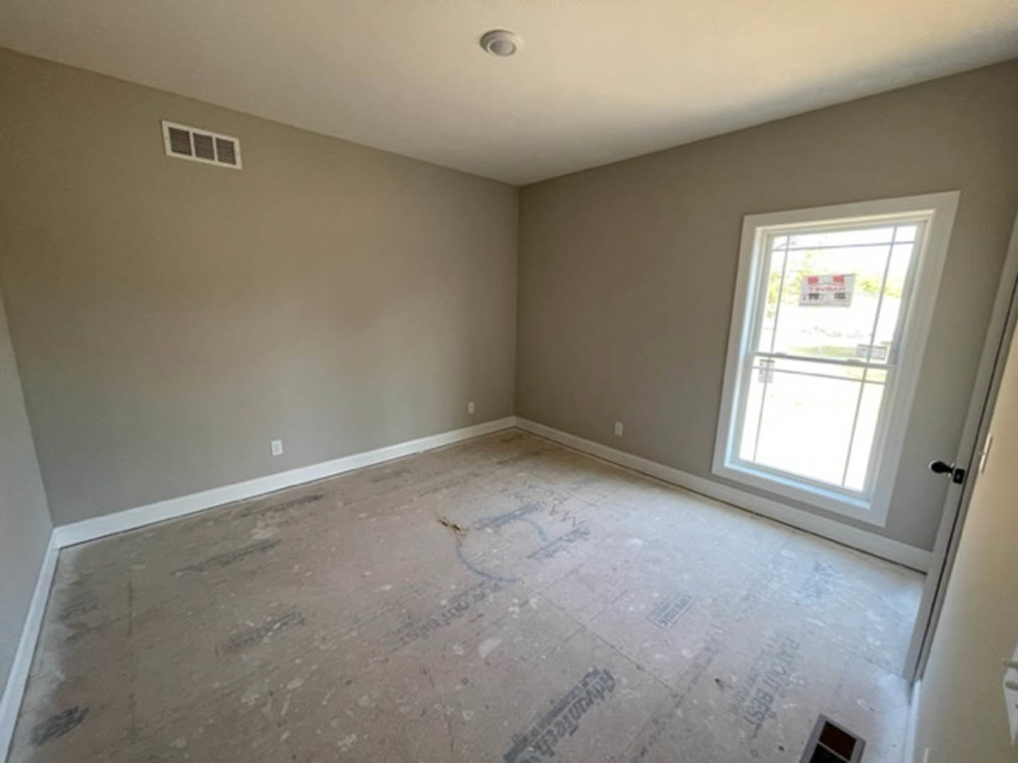 Sunlit room with large window, light-colored tile flooring, white plaster walls, wall vent, and circular fixture on floor