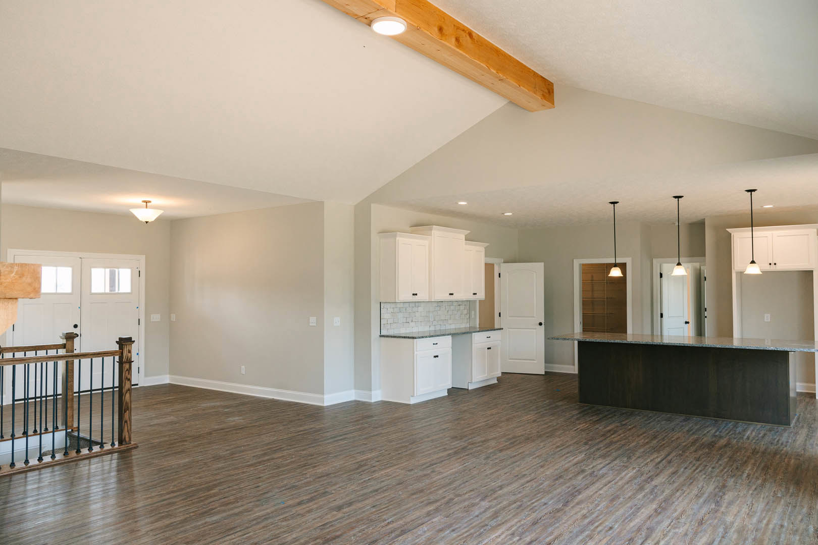 Spacious kitchen with white cabinets, central island, wood flooring, wooden railing with black metal rods, white door with black knobs, and ceiling light fixture