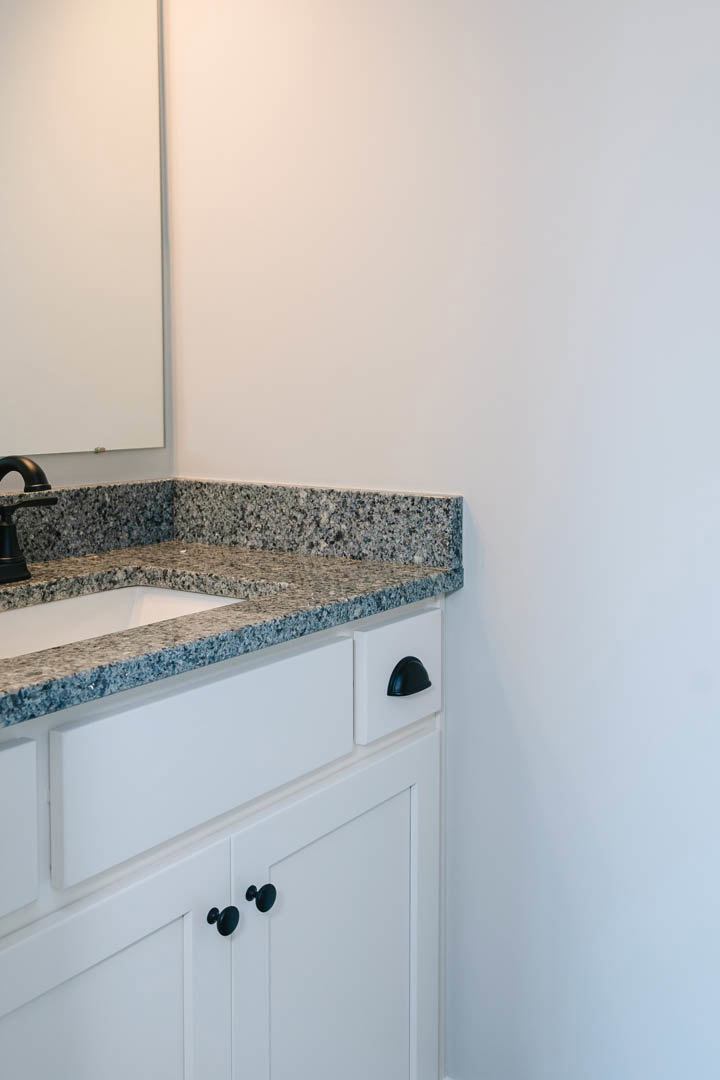White bathroom sink with chrome faucet, rectangular mirror above, white wall with black trim, black cabinet knobs, and white countertop