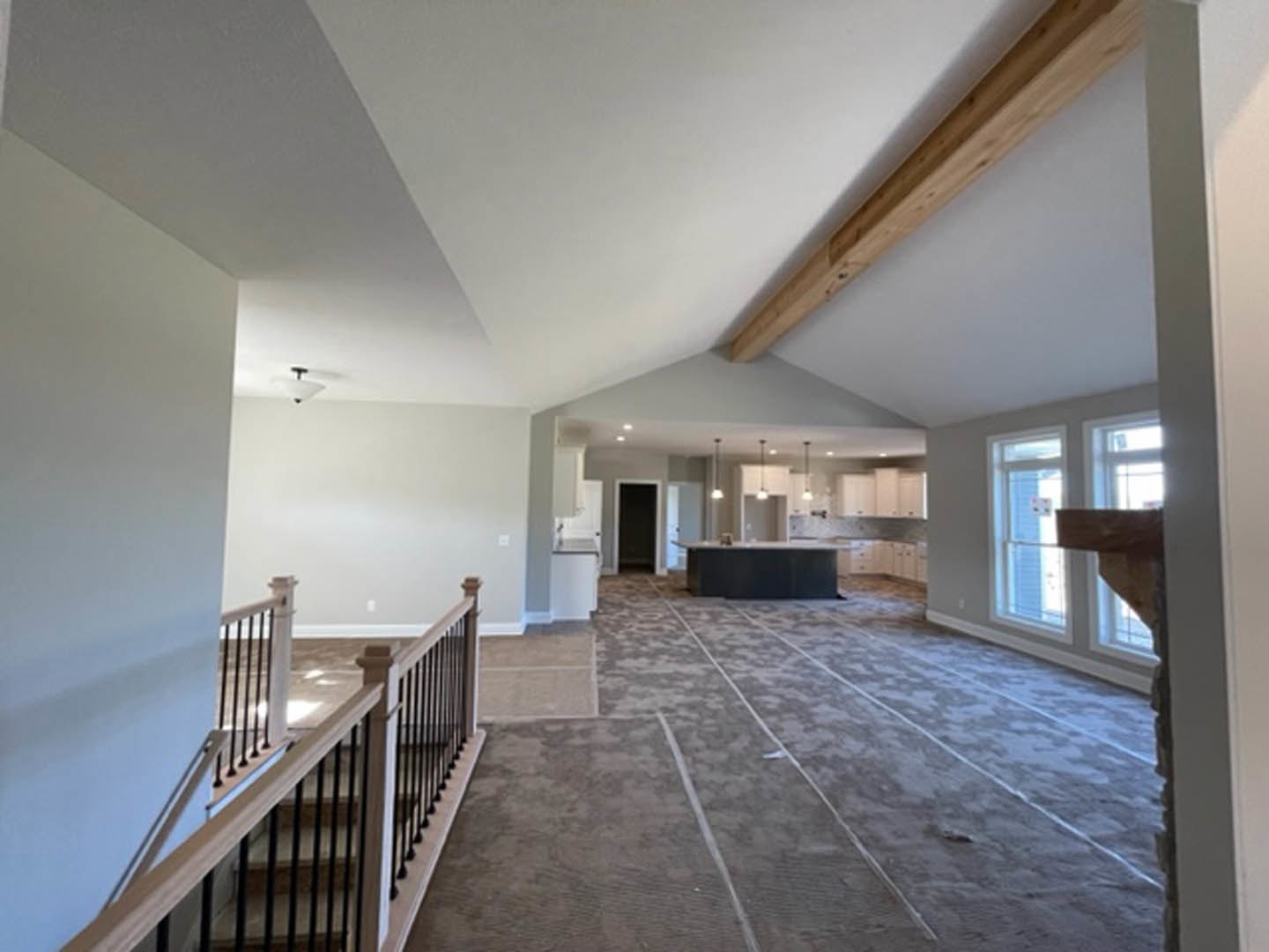 Open-concept room featuring a modern kitchen with a central island, black metal staircase with matching railings, exposed wooden ceiling beam, light plaster walls, and large