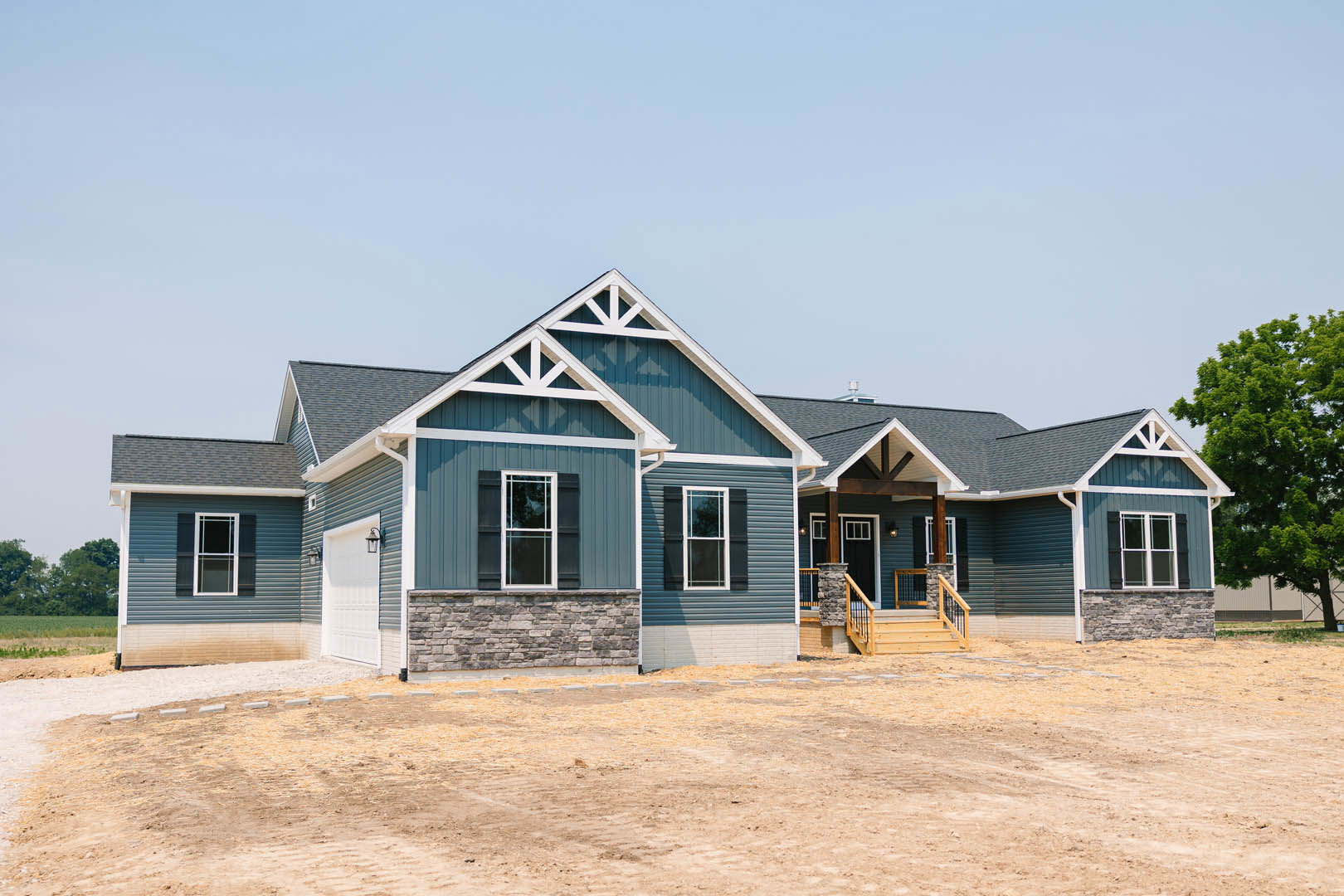 Two-story home with stone wall exterior, wooden stairs, white-framed window, surrounded by dirt yard and tree in the background