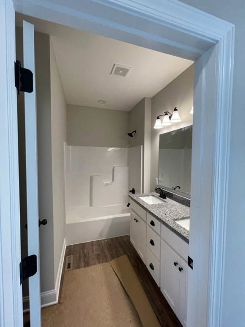 Bathroom with freestanding tub, white sink vanity, light gray tile floor, three-bulb wall sconce, white walls, ceiling vent, and plush carpet visible in foreground.
