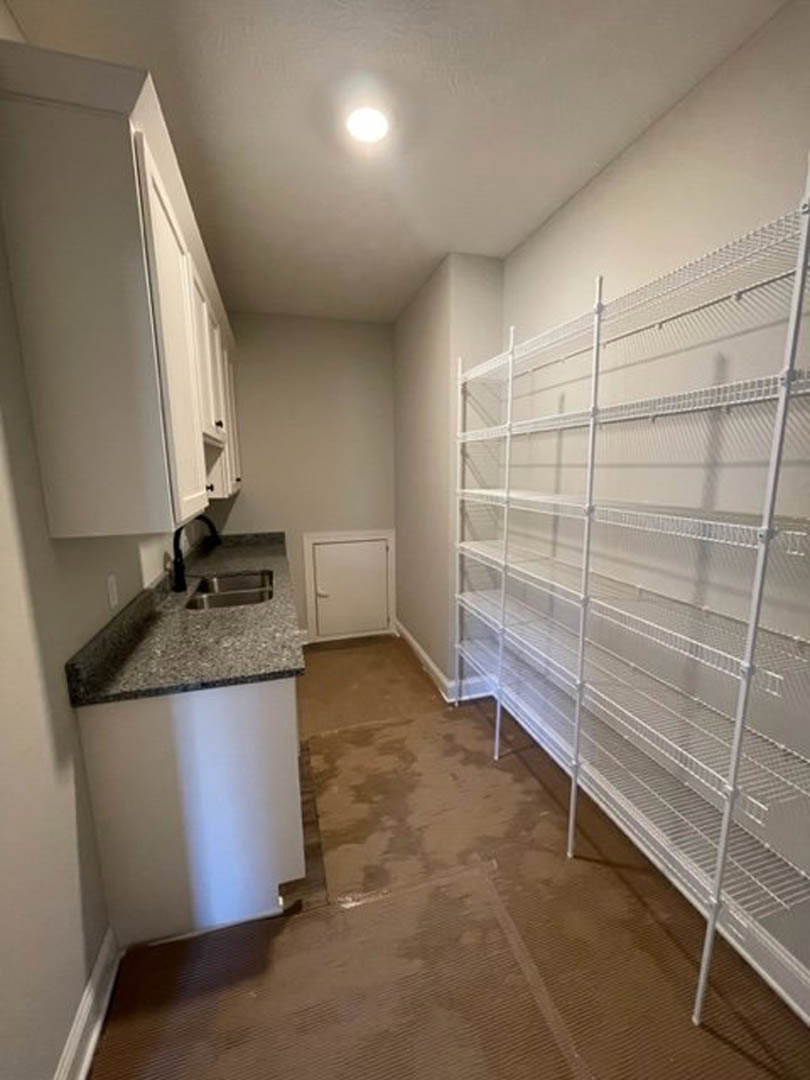 Empty laundry room with white built-in shelves, white door with silver handle, light-colored flooring, and neutral walls