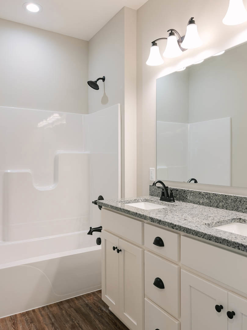 White bathroom with granite countertops, black faucet, white cabinets, rectangular mirror, freestanding bathtub, and tile walls.