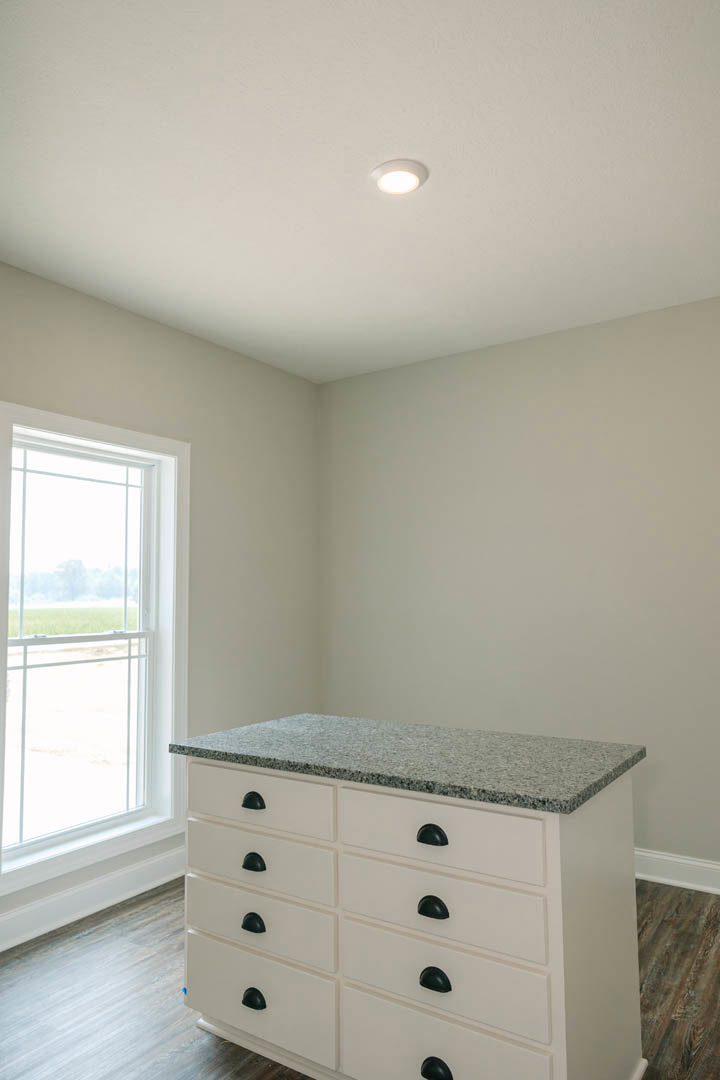 Quartz kitchen countertop with white cabinetry and black handles, large window overlooking grassy field, ceiling light fixture, neutral wall finishes