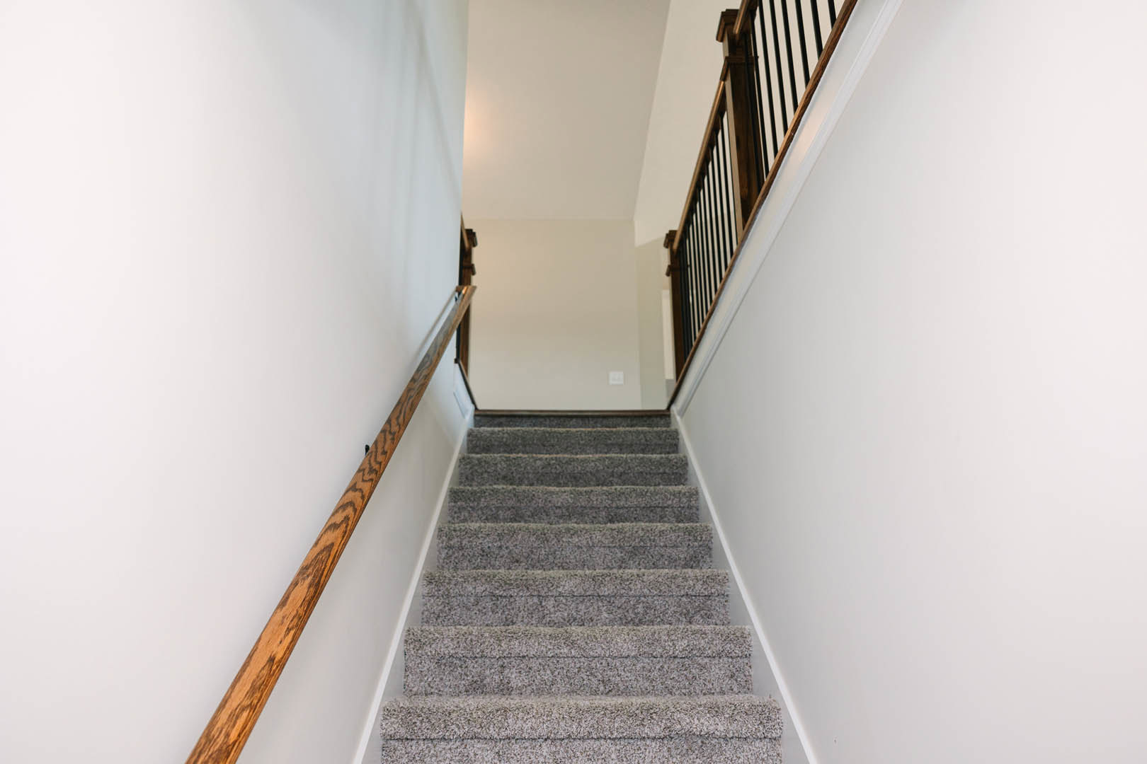 Carpeted staircase with wooden handrail, white plaster walls, and a wooden shelf along the landing