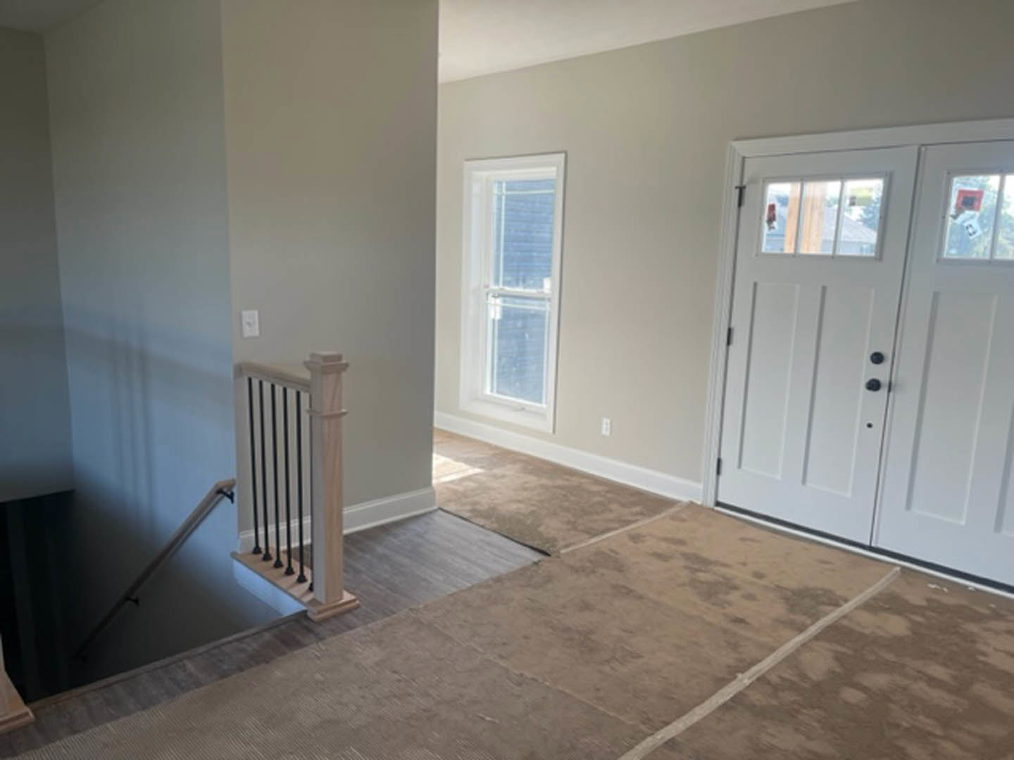 Hallway with white door featuring black knobs, wood flooring, white plaster walls, staircase with dark handrail, and window adjacent to stairs