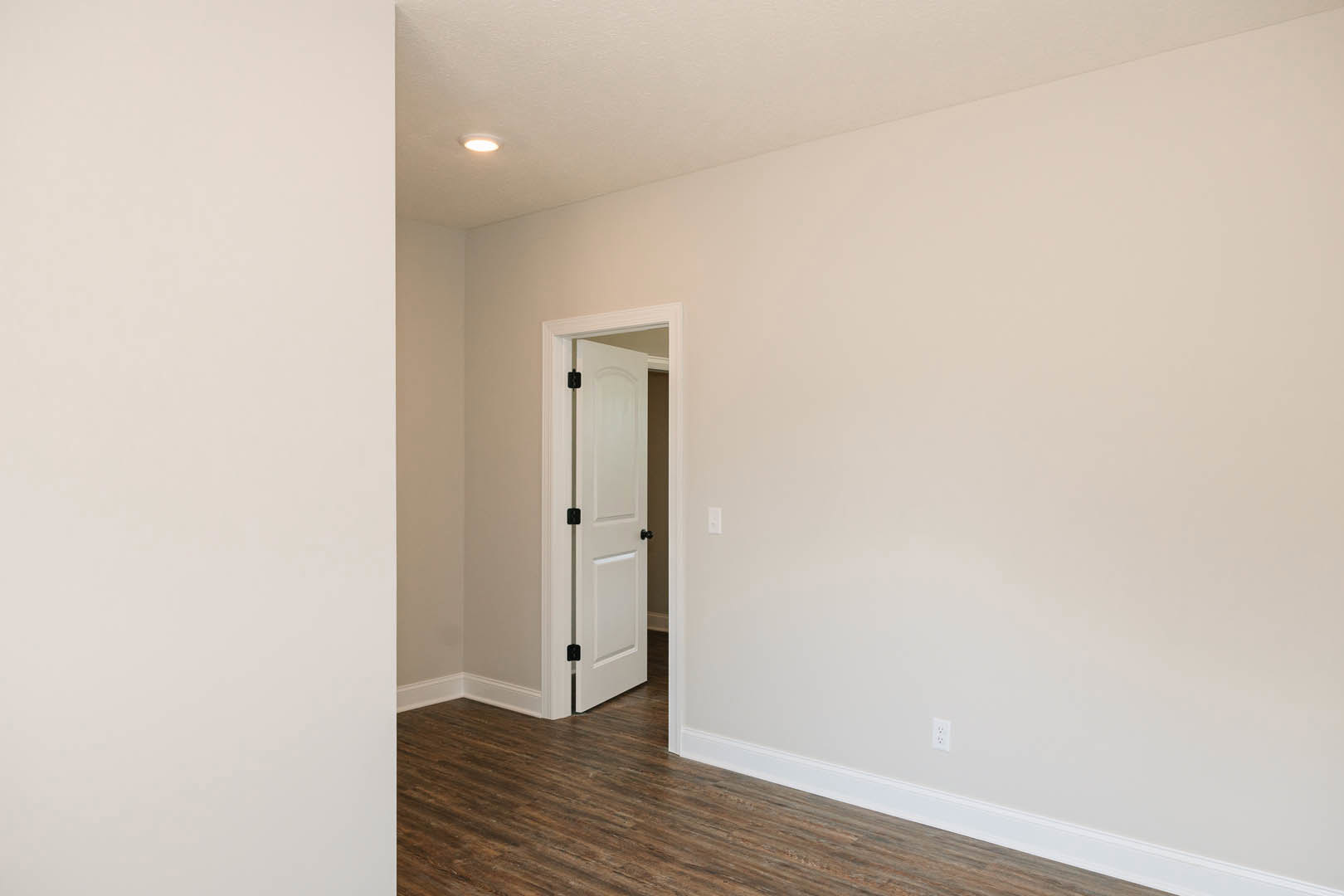 White-painted room with open black and white door, wood laminate flooring, white plaster walls, and simple molding.