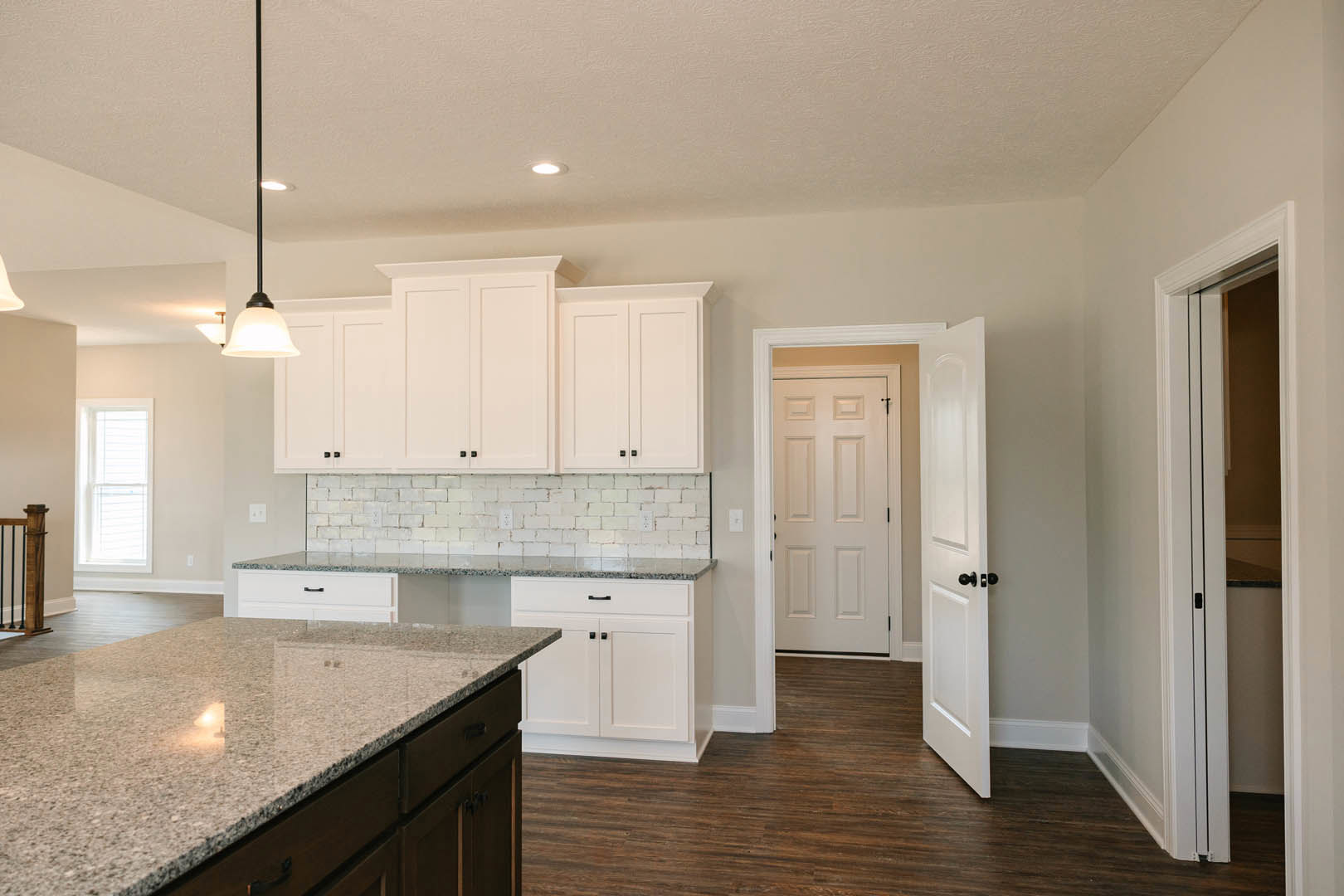 White kitchen with marble countertops, white cabinetry, stainless steel sink, tile backsplash, and light hardwood flooring.