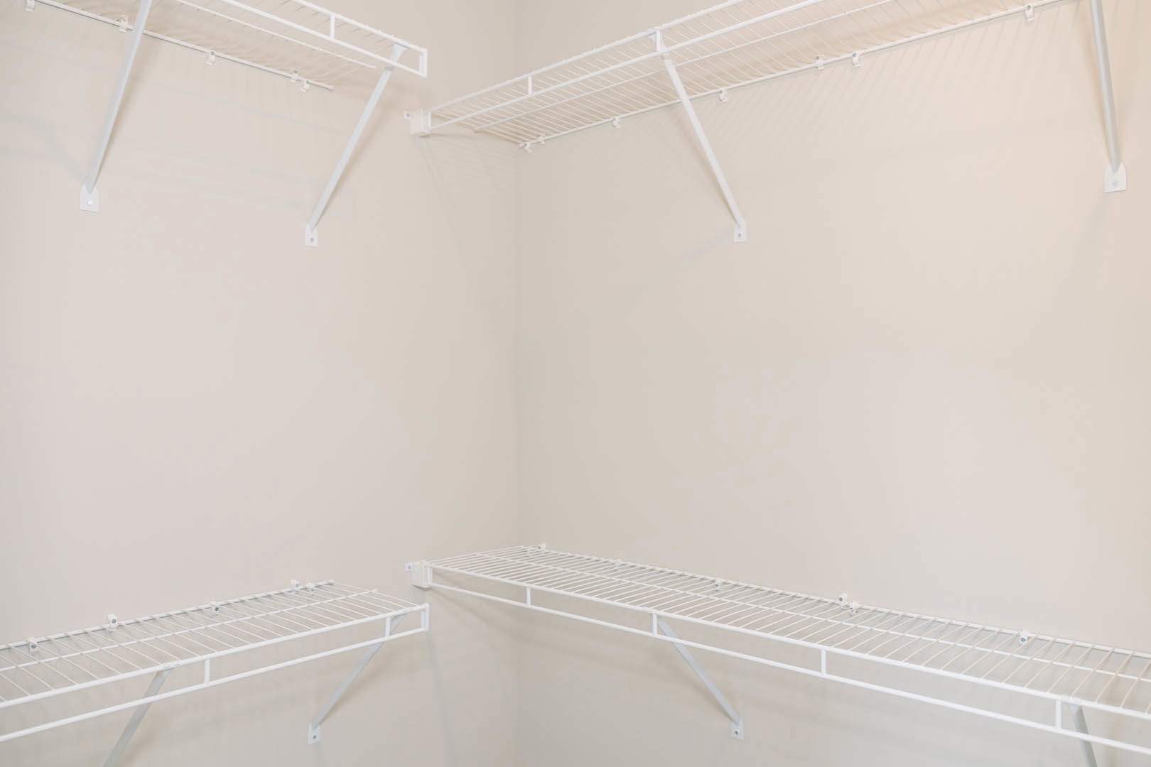 White built-in shelving unit with metal clothes rack mounted on a white plaster wall in a minimalist room.