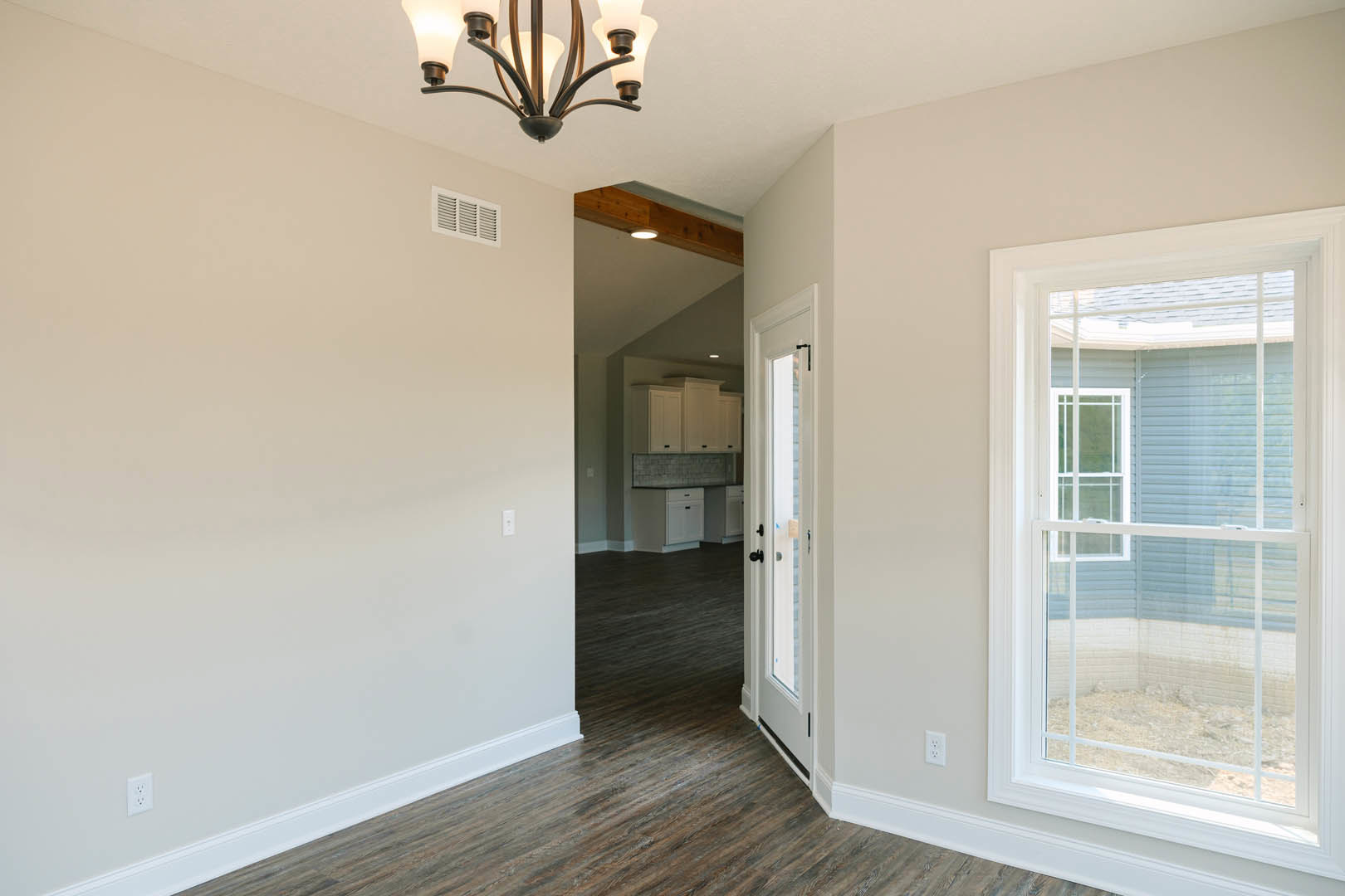 Hallway with light wood flooring, white walls, white-framed window, white door, white cabinet with black handles, decorative chandelier, wall vent, and crown molding