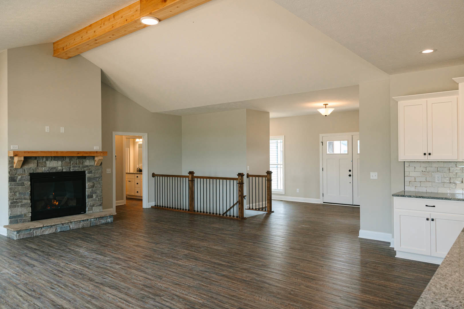 Spacious living room featuring wood flooring, active fireplace with stone surround, wooden railing with black metal balusters, white door with glass window, partial view of