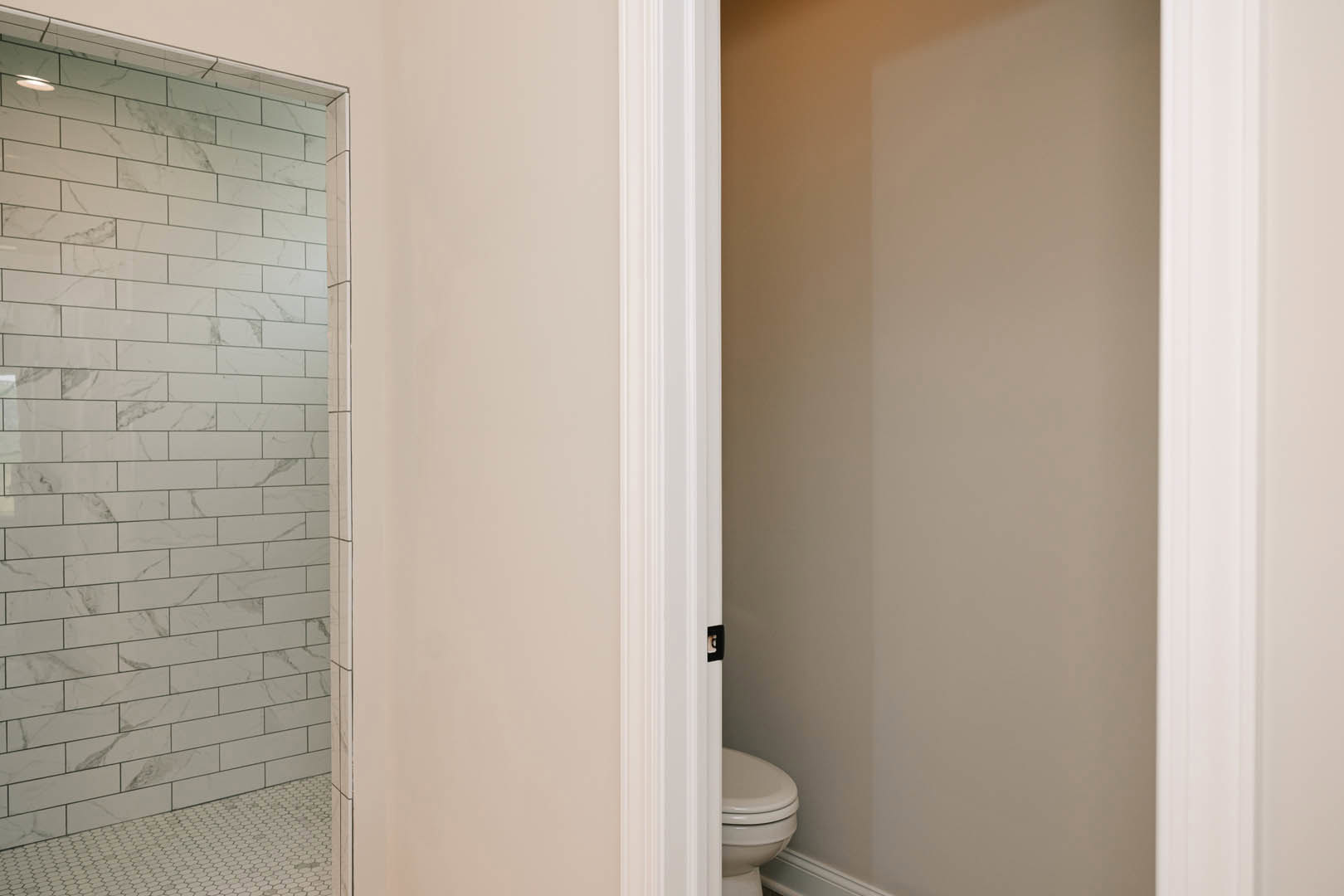 Bathroom with white tile walls and floor featuring black grout lines, modern toilet, glass shower enclosure, black door, and wall-mounted mirror.