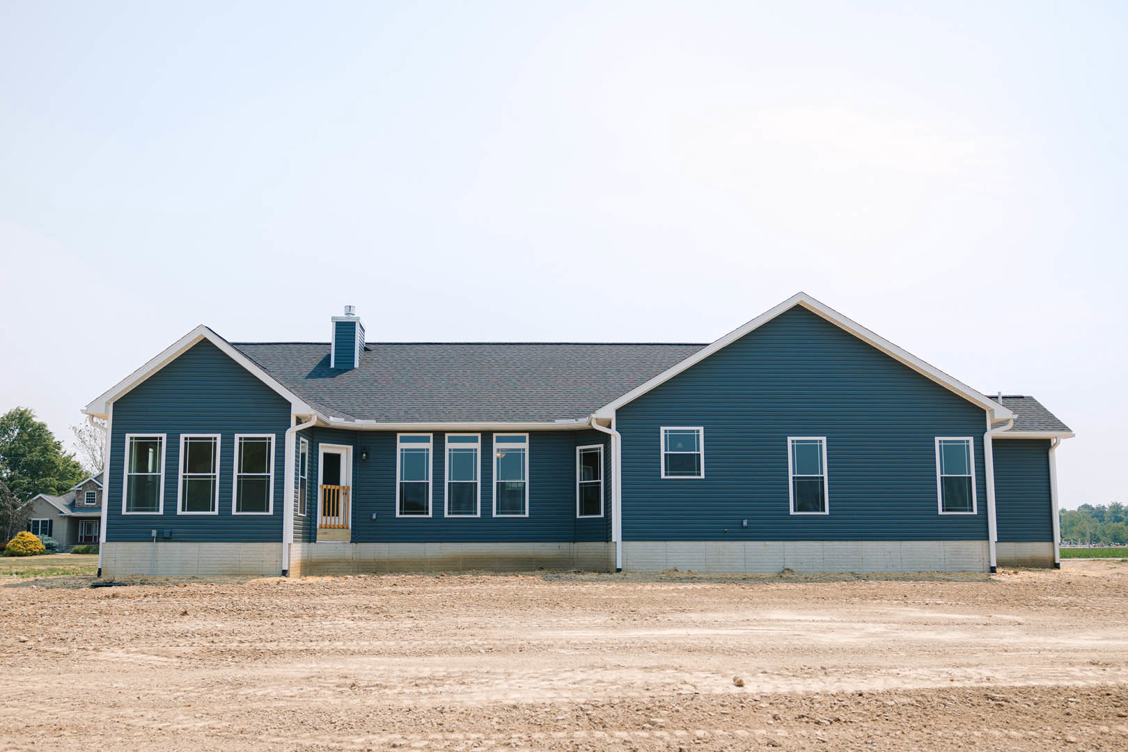 Blue house with white trim and illuminated window, surrounded by dirt road and open field under clear sky