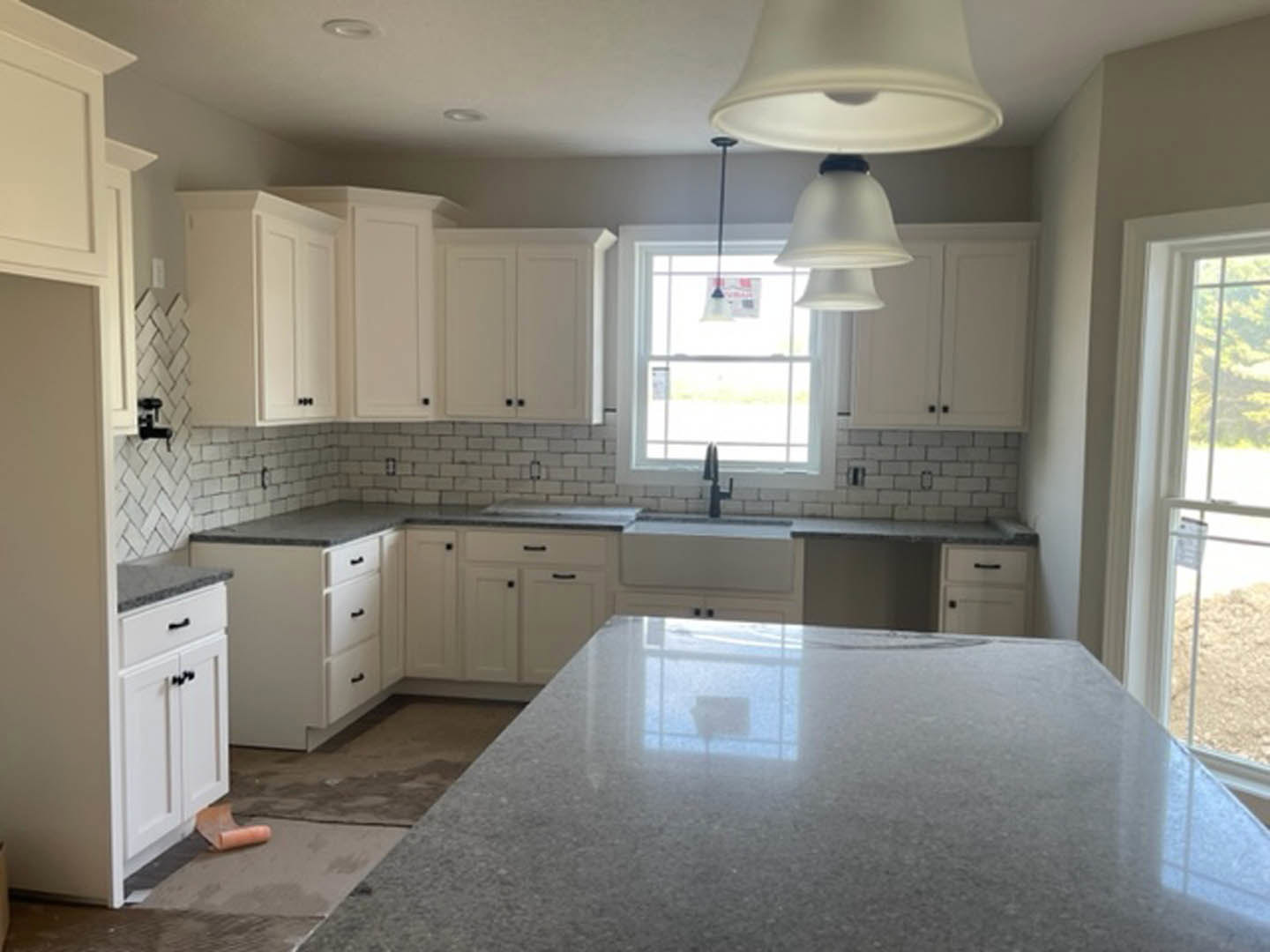 White kitchen cabinets with polished marble countertops, stainless steel appliances, pendant lights, and a window providing natural light.