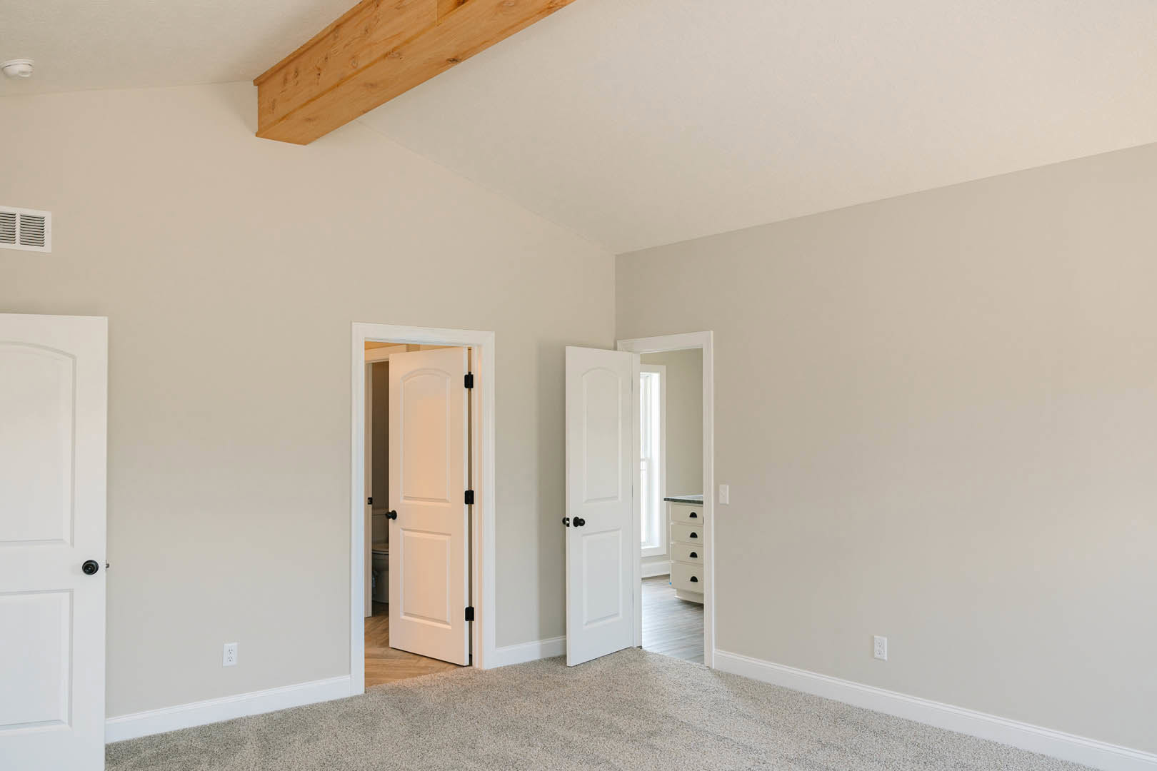 White walls, wooden ceiling beam, open white door with black knobs, carpeted floor, simple molding