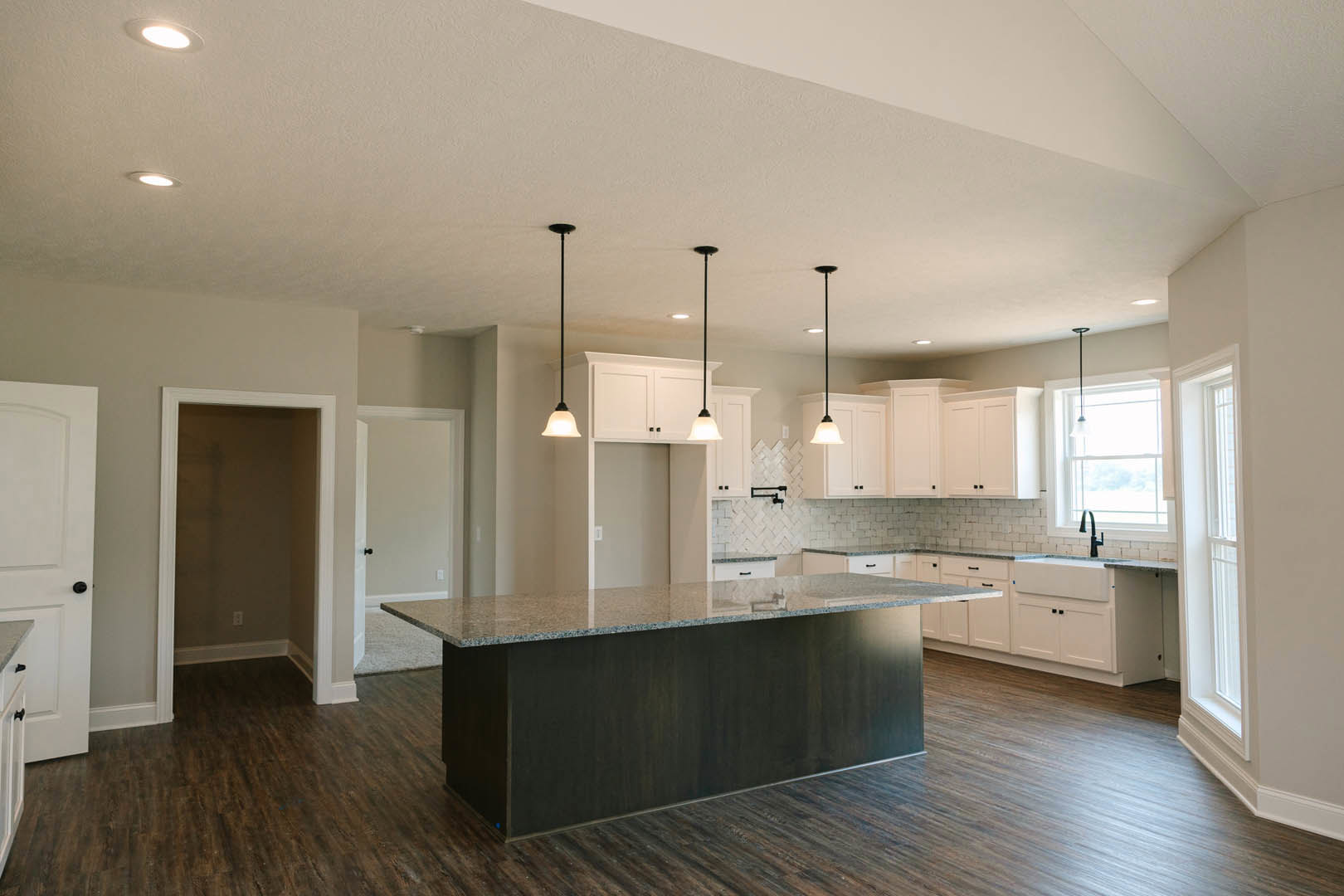 Kitchen with white shaker cabinets, central island with light stone countertop, stainless steel sink, tile backsplash, and large window providing natural light