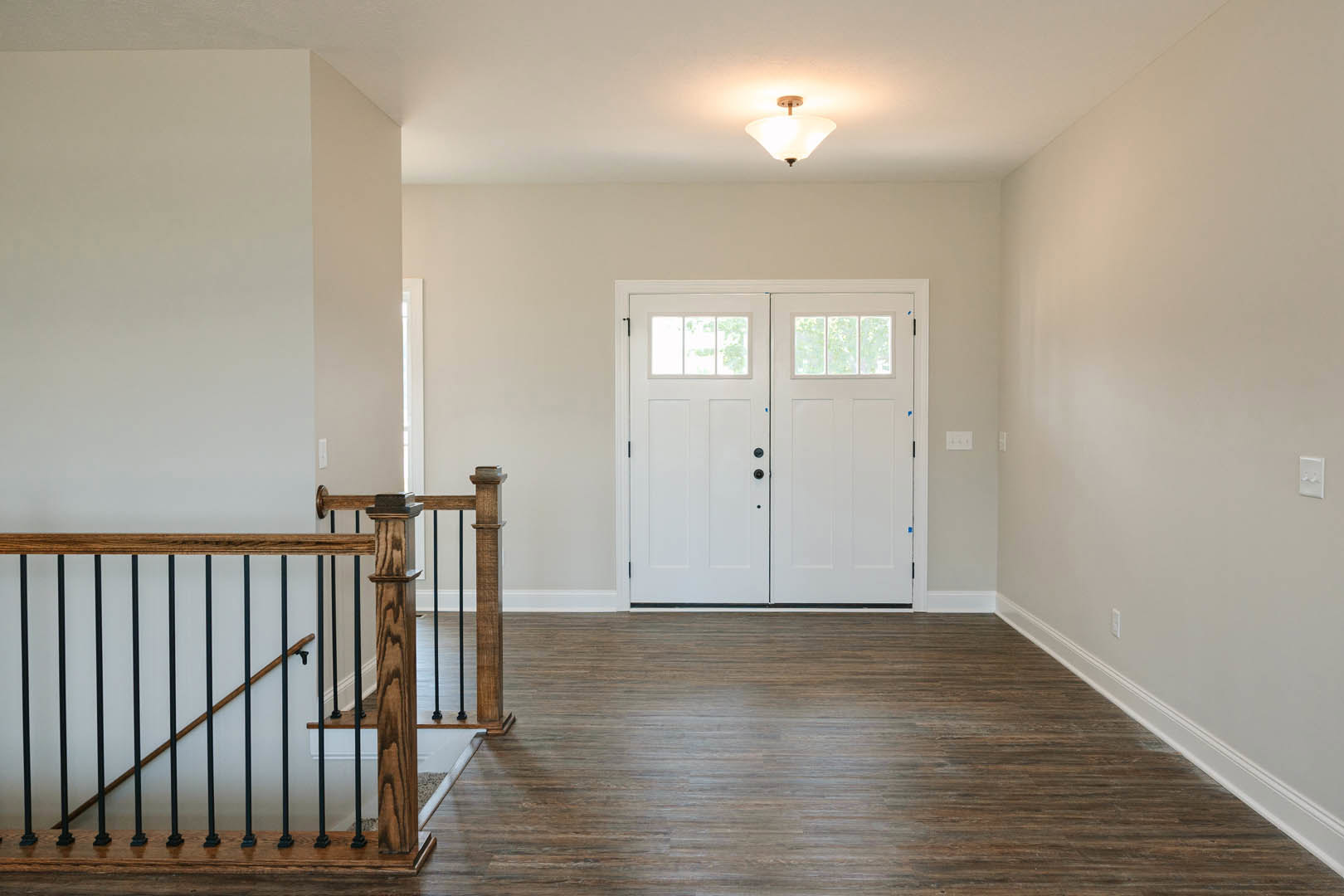 Hallway with wood flooring, white trim, double white doors with glass panes, wooden railing with black metal balusters, ceiling light fixture, white walls