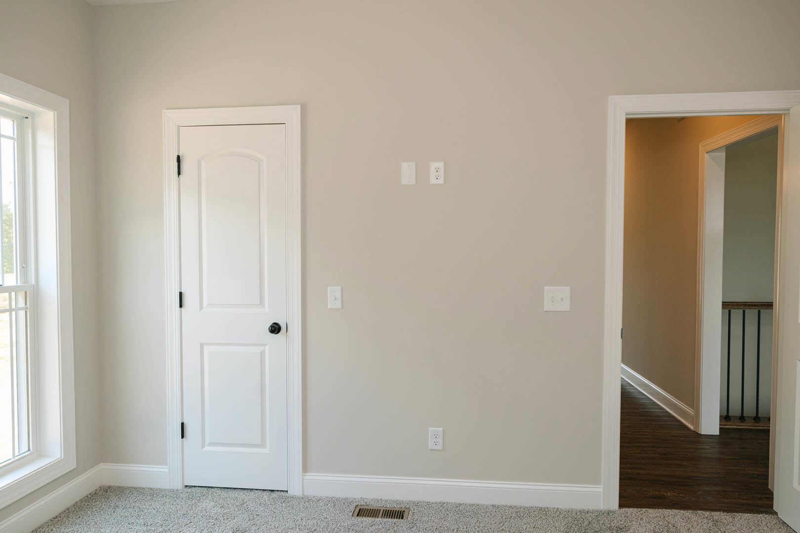 White paneled door with black knobs set in a white wall, adjacent to a doorway, wood flooring visible in foreground