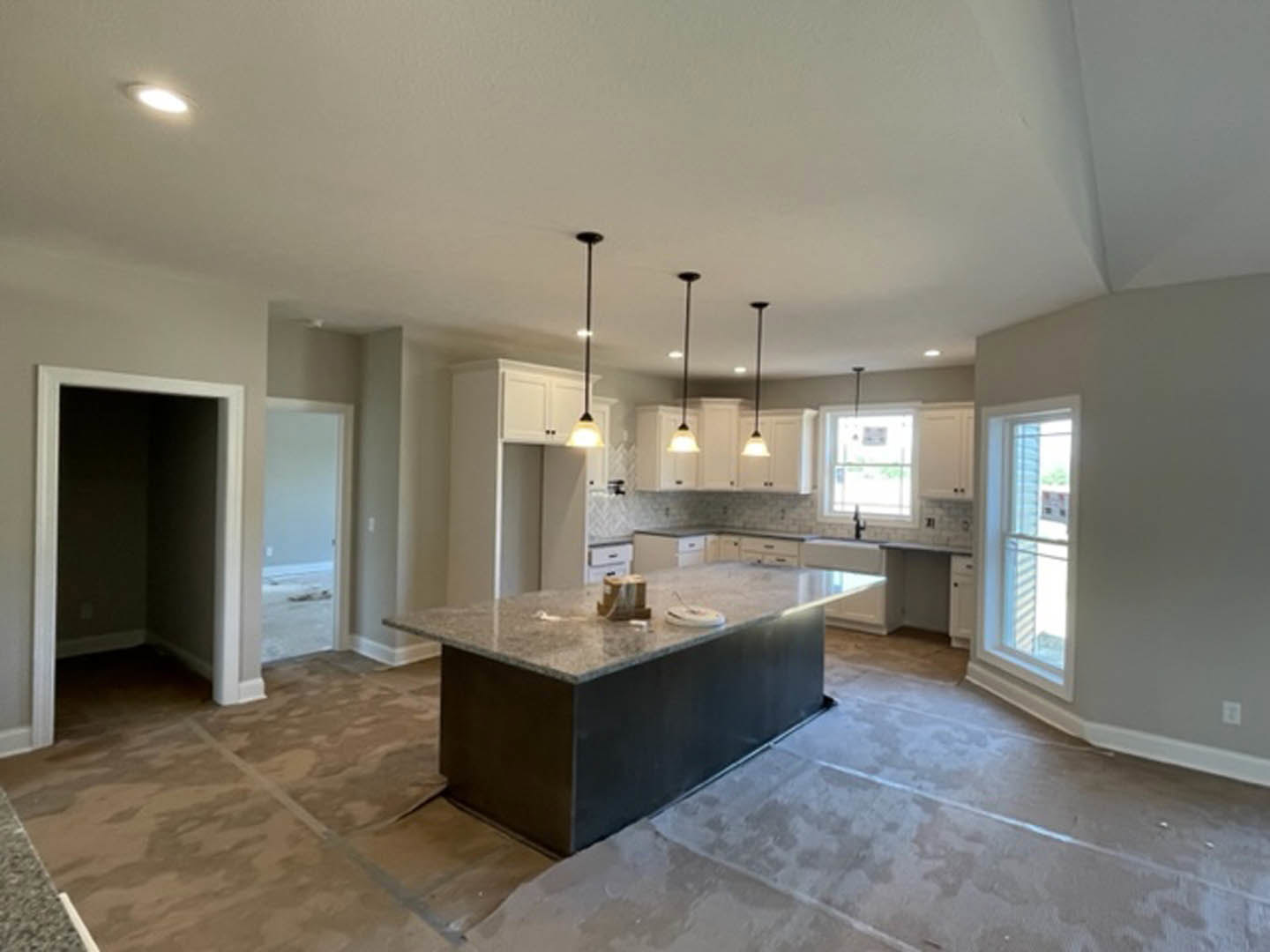Modern kitchen featuring a central island with white cabinetry, tile flooring, stainless steel sink, open doorway, and large window with a white frame.