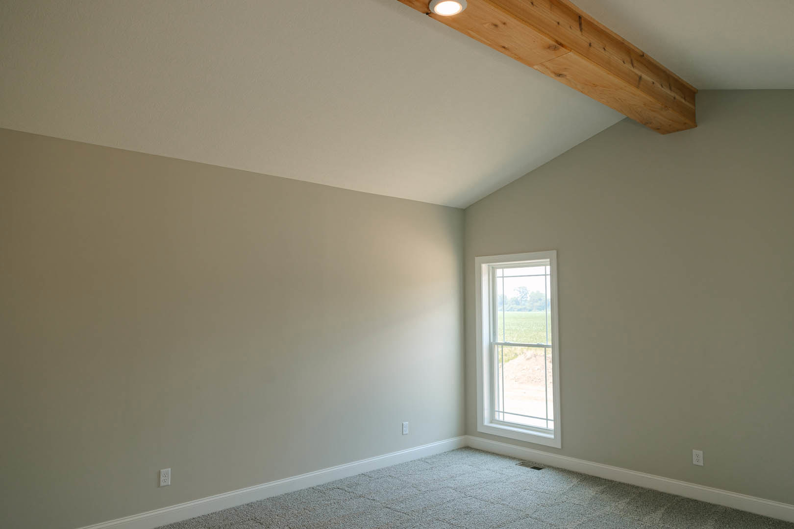 Carpeted room with a large window overlooking a field, exposed wooden ceiling beam, white ceiling with recessed light fixture, plaster walls and decorative molding