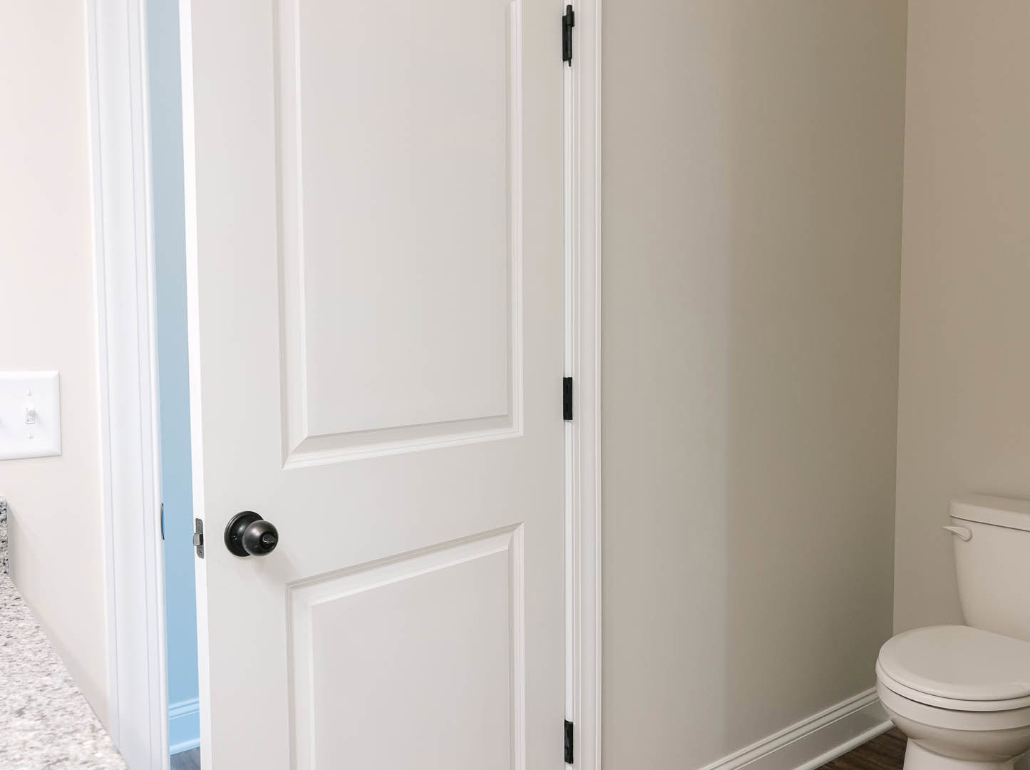 White paneled door with black trim and black hardware, adjacent light switch on white tiled bathroom wall