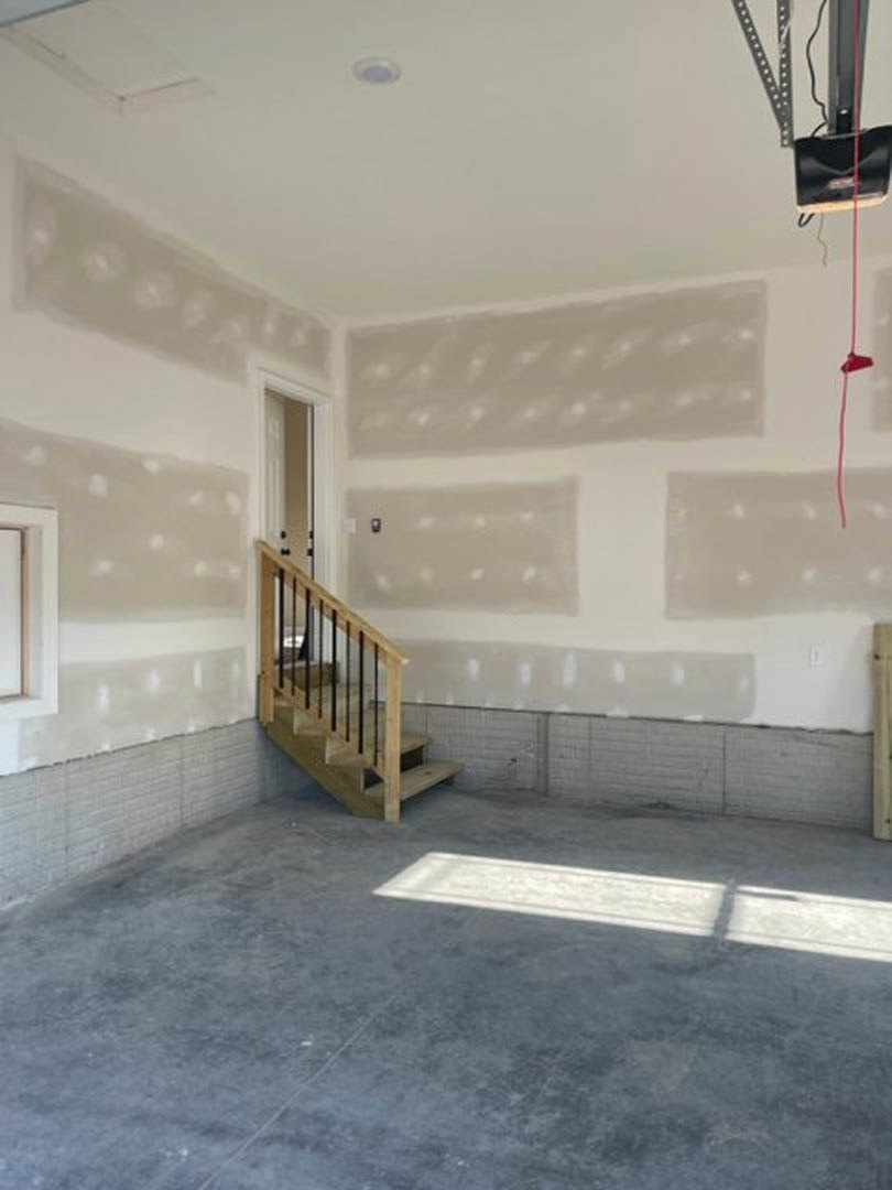 Open-concept room featuring a wooden staircase with black metal railings, concrete floor, white plaster walls, and large windows.