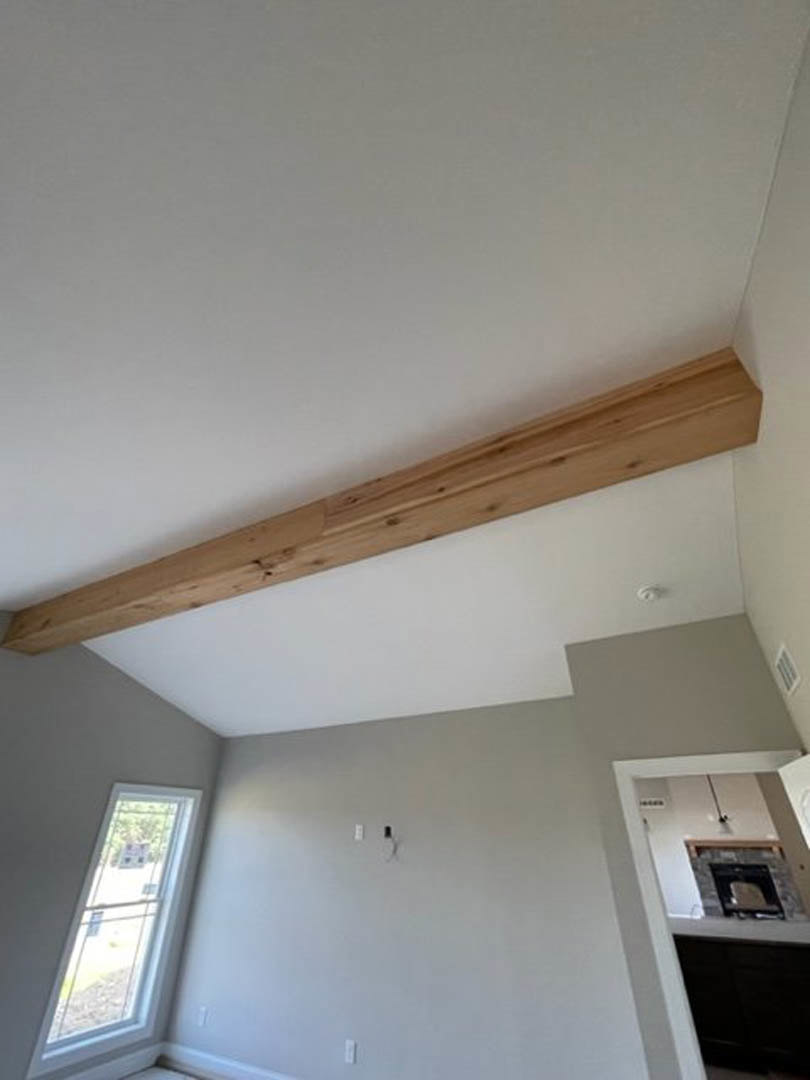 Exposed wooden ceiling beam above plaster walls, window with sign, fireplace with stone surround, molding details, plywood finishes