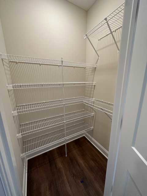 Closet with white shelves and dark hardwood floor, white walls, and a white door