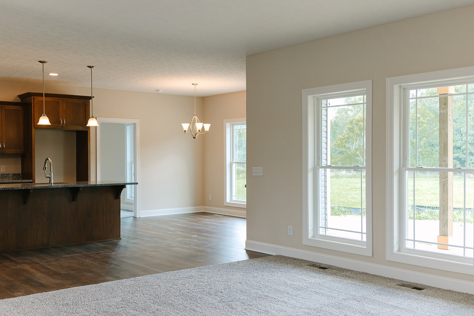 Open kitchen with stone countertop, white cabinetry, large windows overlooking grassy yard, chandelier hanging from ceiling, light carpet flooring