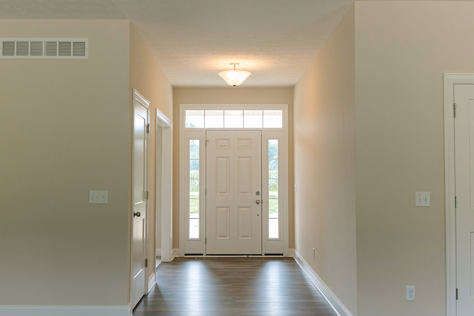 Hallway with white paneled doors, ceiling light fixture, light wood flooring, wall-mounted light switch, and vent near baseboard