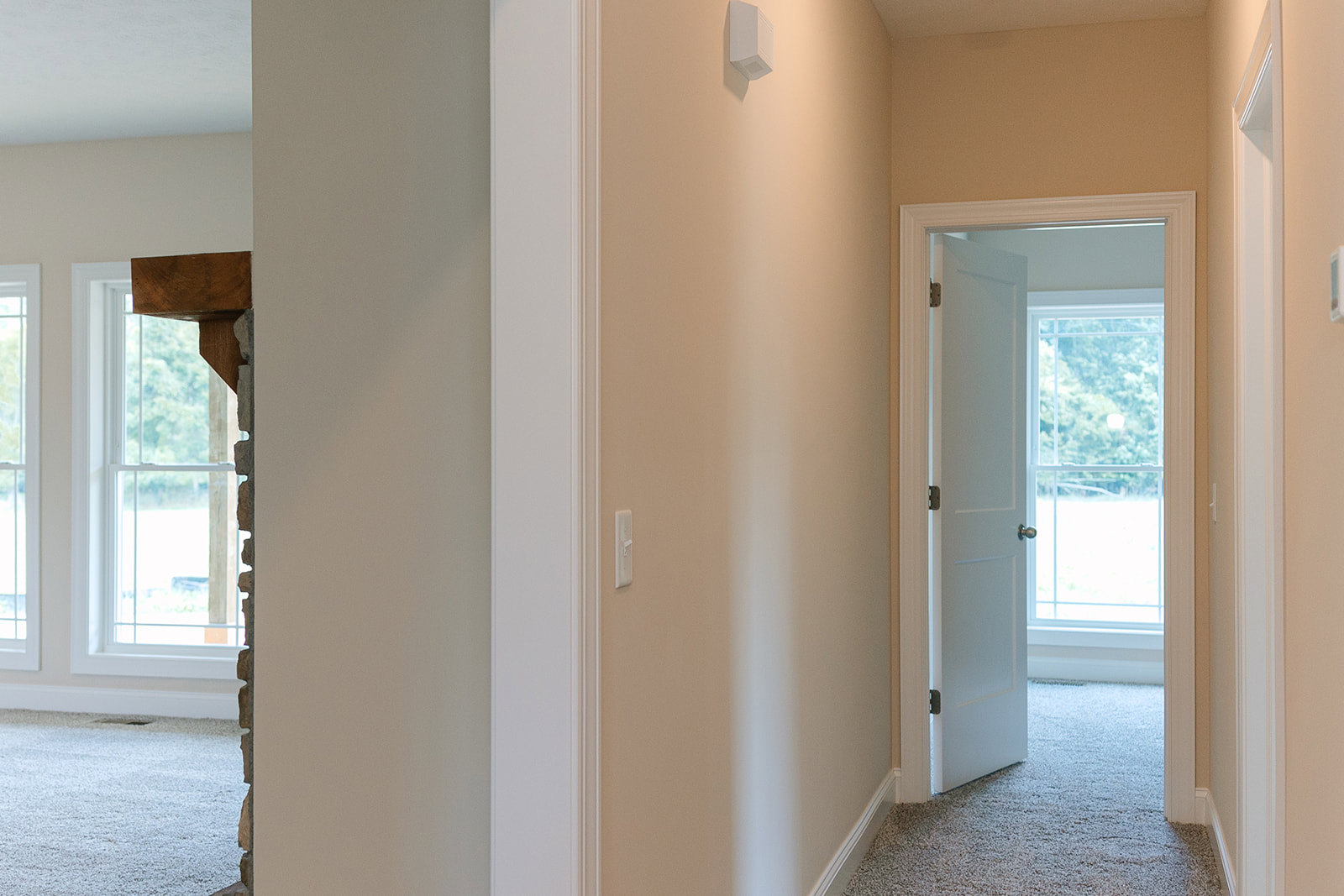 Hallway with white walls, white door featuring a silver knob, light switch, carpeted floor, ceiling vent, and window visible through open doorway