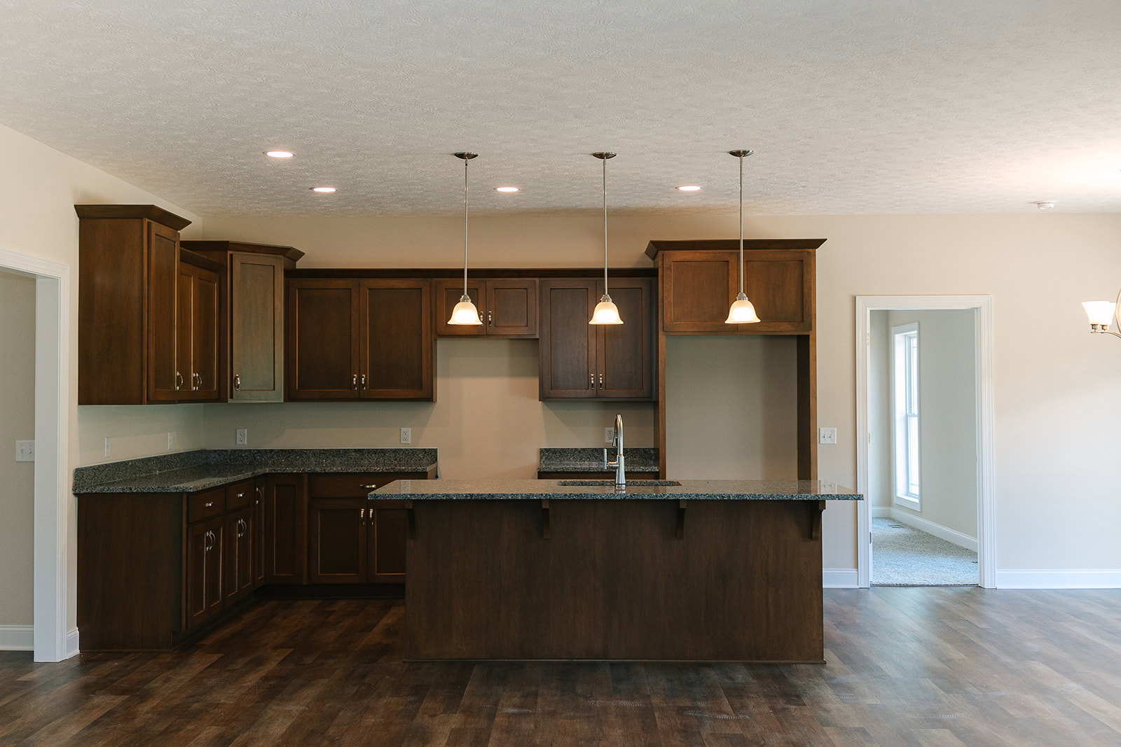 Modern kitchen featuring a central island with stone countertop and built-in faucet, white cabinetry, tiled floor, large window set in a white wall, recessed ceiling lights, and