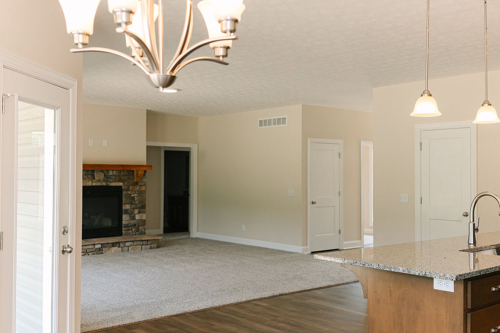 Living room featuring a stone fireplace with a wood beam mantel, marble countertop with wood base, white door with silver knob, black rectangular fireplace insert, and chandelier