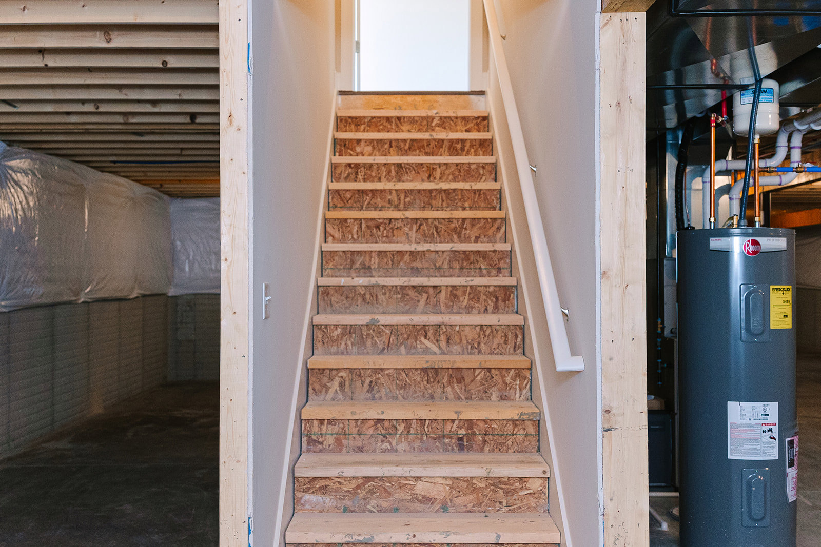 Wood plank staircase with open door, white walls, metal handrail, and composite material accents