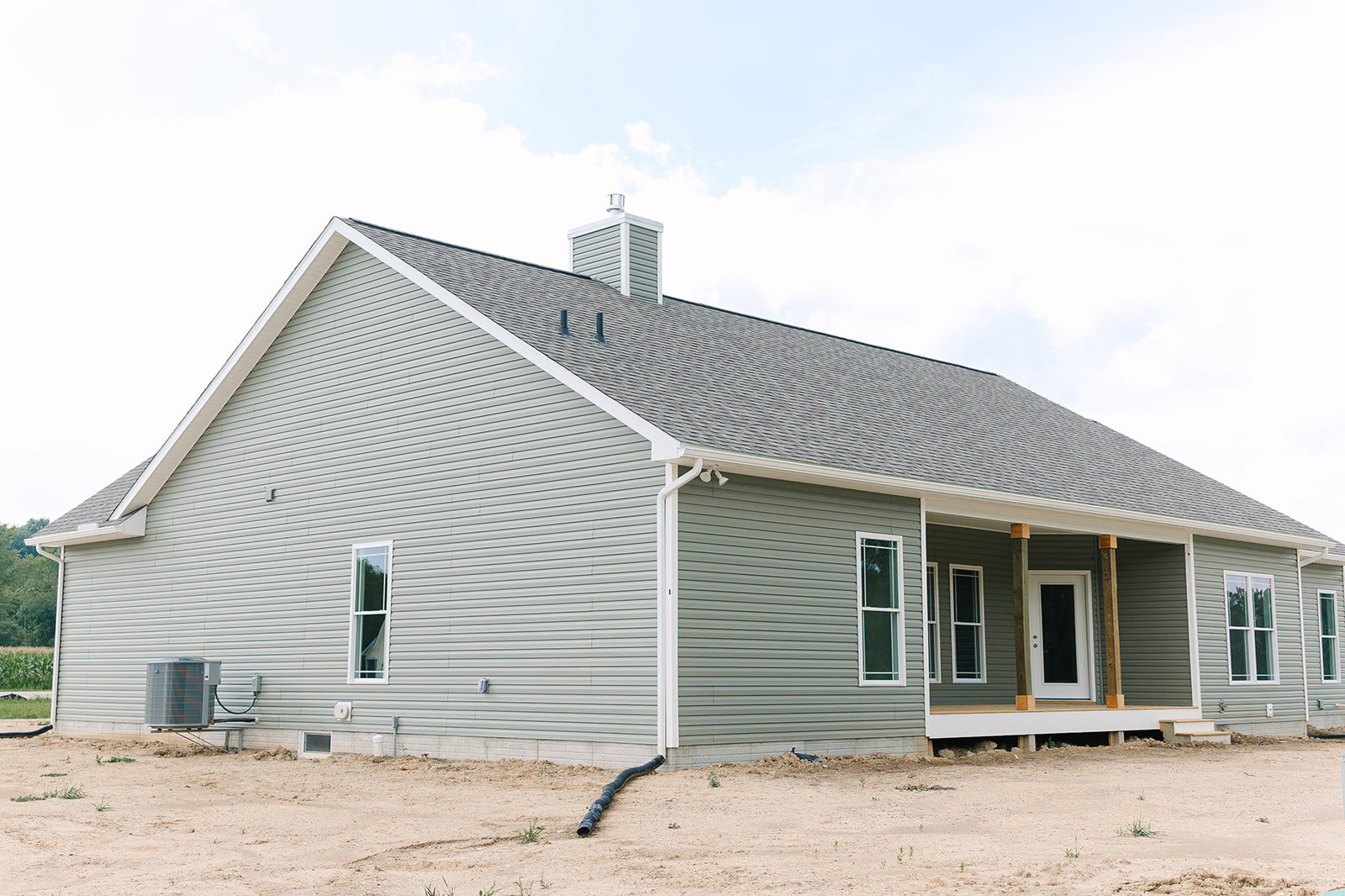 Partially built house featuring a spacious covered porch, exposed chimney, white-framed window, white door with glass panel, large air conditioner unit on a truck, and a long black