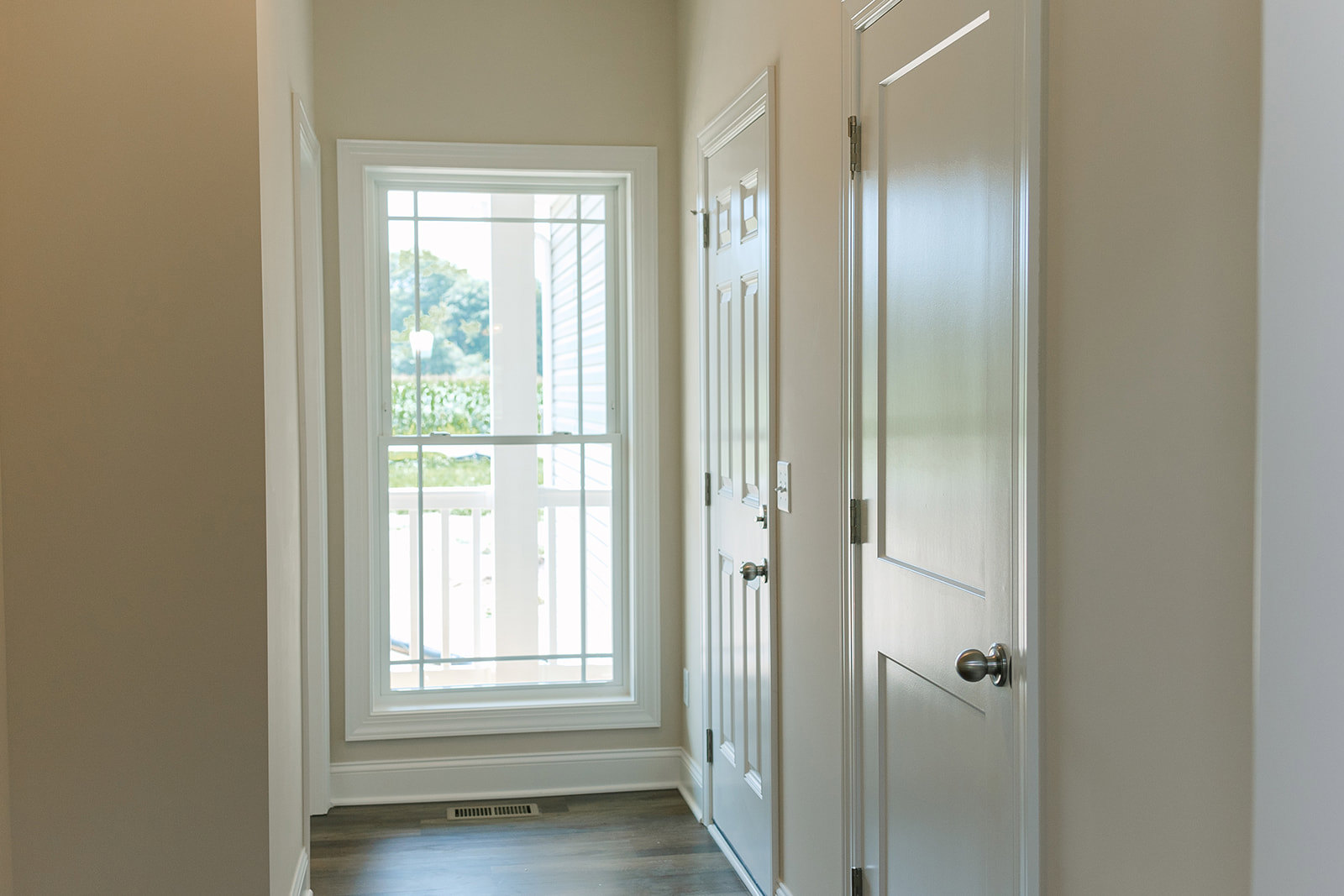Hallway with light wood flooring, two white paneled doors, frosted glass door, white framed window, silver door knob, and wall vent