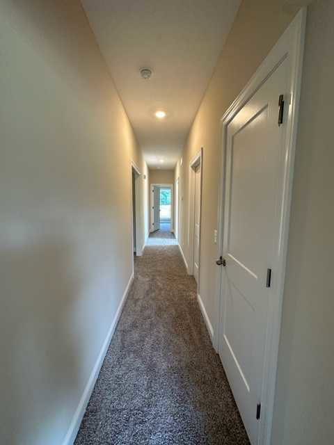Long hallway with white walls, multiple white paneled doors, and light beige carpet flooring