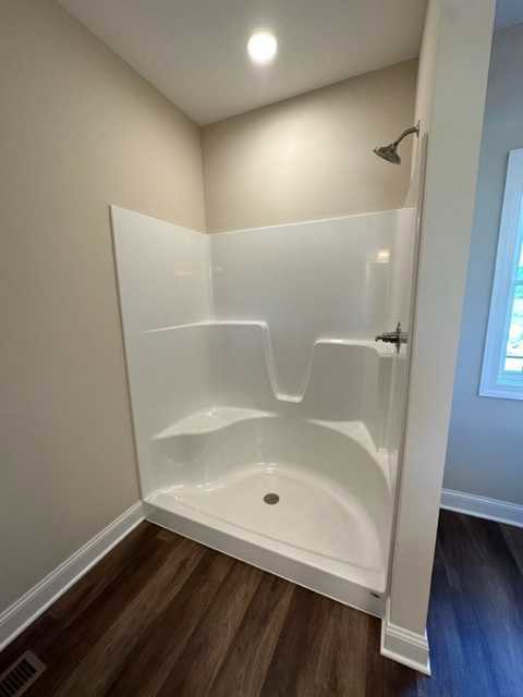 White tile shower with glass door, blue wood floor and white trim, bathroom wall with plumbing fixtures