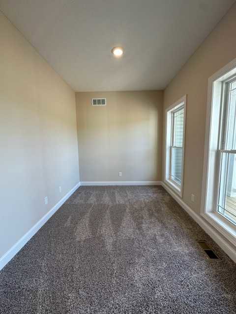 Carpeted room with white-framed window, white door handle on white door, wall and floor vents, neutral walls and ceiling