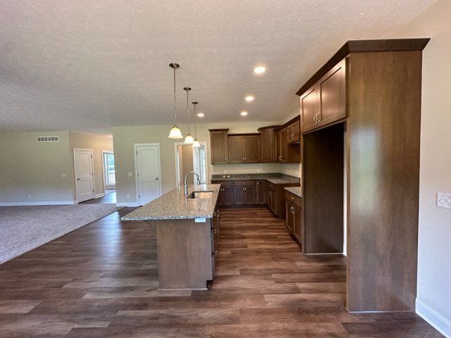 Kitchen with hardwood flooring, central island featuring built-in sink, white plaster walls, and recessed ceiling lighting