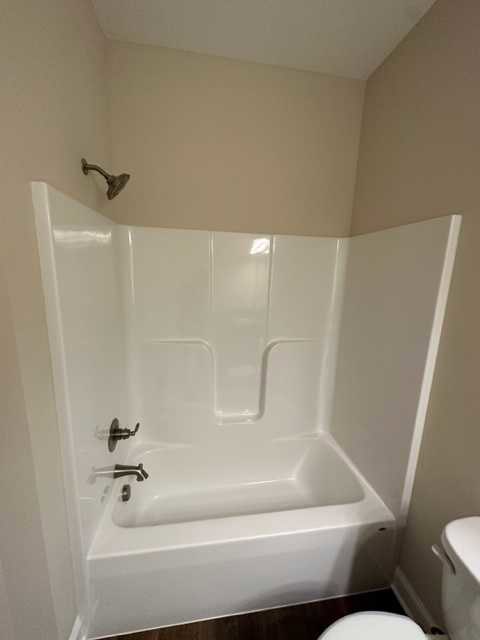 Freestanding white bathtub beside a toilet, surrounded by light tile walls and floor in a modern bathroom