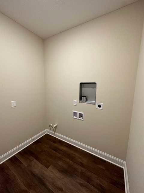 White wall with a recessed square shelf holding a can of food, wood laminate flooring, and white baseboard in a corner of a residential interior.