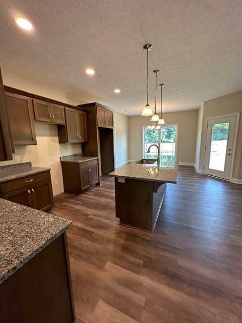 Open kitchen with light wood flooring, brown cabinetry, stone countertop with built-in sink, glass-paneled door, and neutral walls