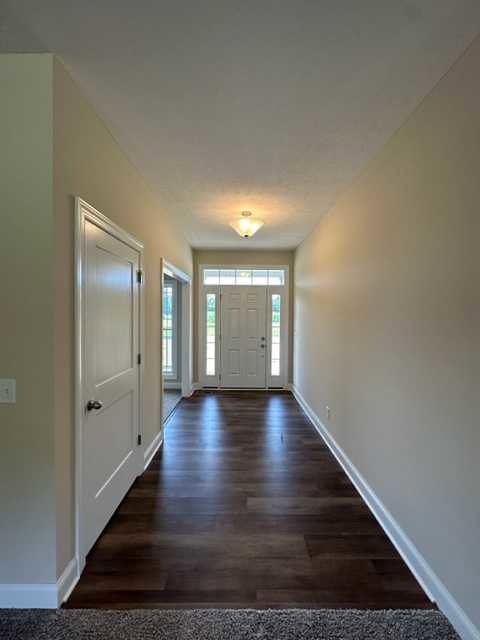 Long hallway with dark wood floors, multiple white doors, and smooth white walls