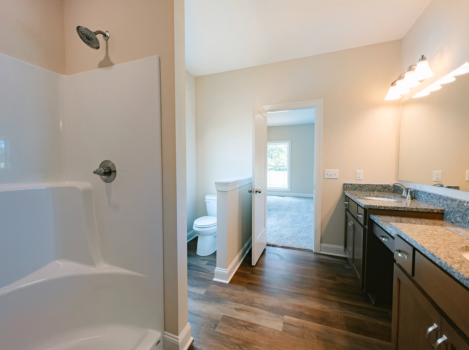 Bathroom with white toilet, rectangular sink on stone countertop, white bathtub with chrome faucet, tiled walls, window with natural light, row of bulb light fixtures above mirror