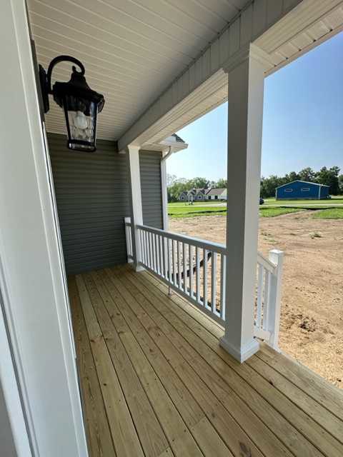 Wooden deck porch with white railing, black lantern mounted beside a close-up white door, exterior window visible, grassy yard and sky in background