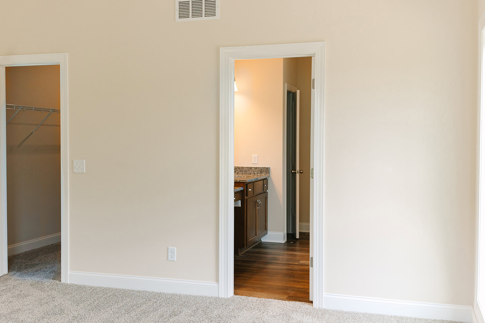 White door with matching frame opening into a room with hardwood flooring, white walls, light switch, and a patterned rug partially visible.
