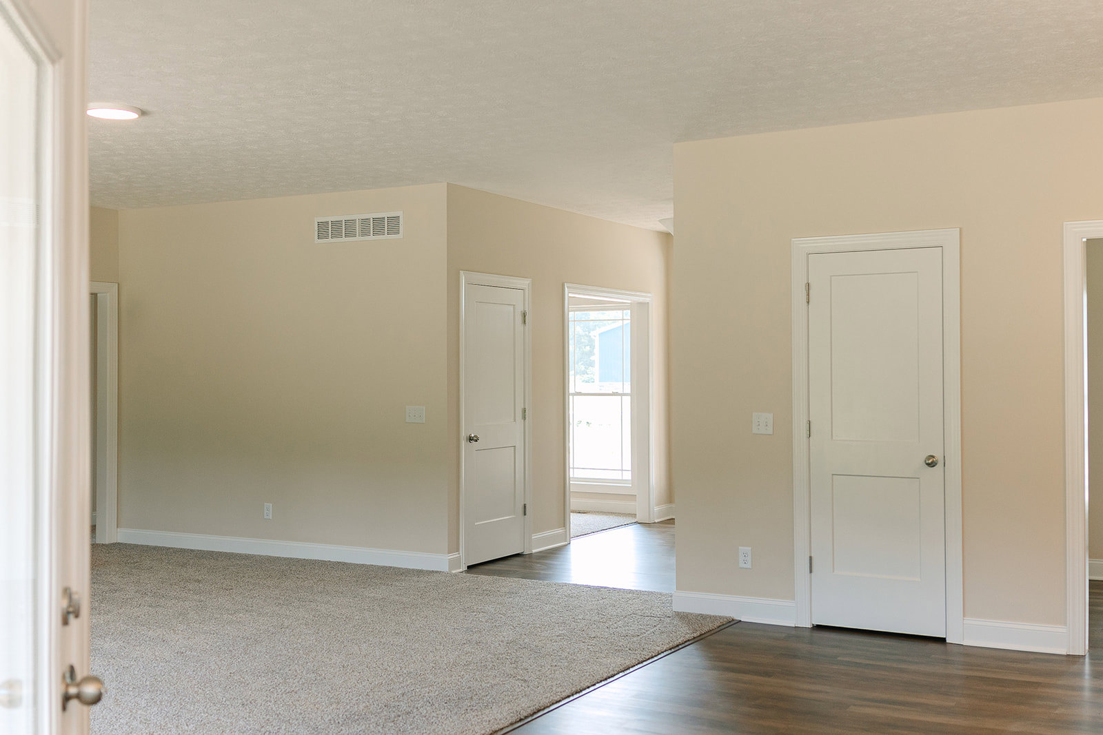 White carpeted room featuring white paneled doors with silver knobs, white-framed window, and smooth plaster walls.